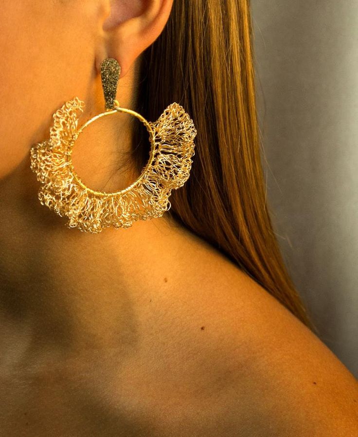 a close up of a woman wearing large gold hoop earrings with filigrees