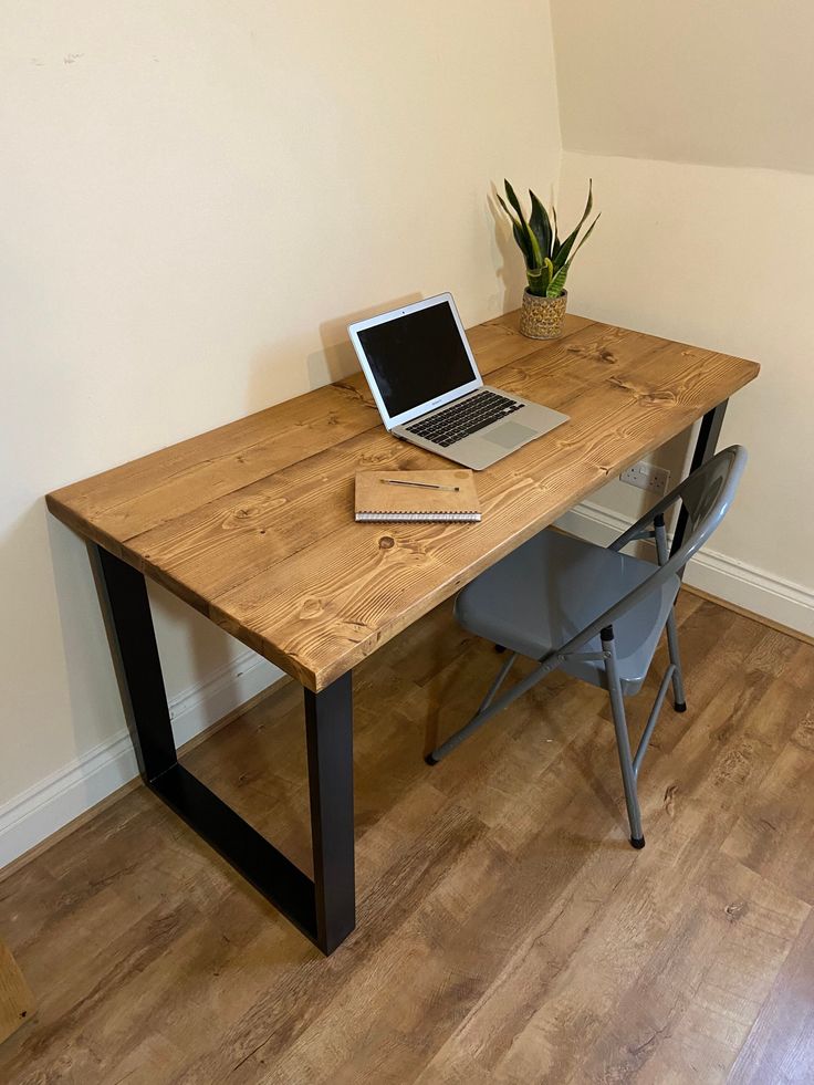 a laptop computer sitting on top of a wooden desk next to a chair and potted plant