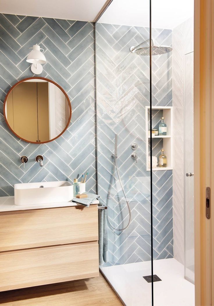 a bathroom with blue and white tiles on the wall, shower head, sink, and mirror