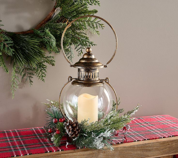 a candle is lit in a glass lantern on a table next to a christmas wreath