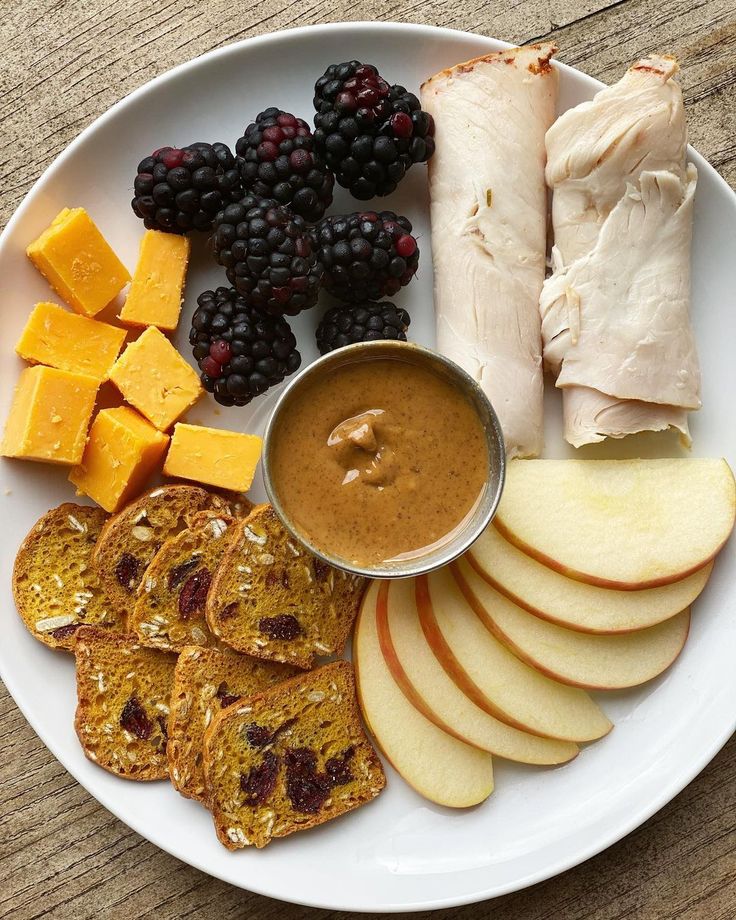 a white plate topped with fruit and crackers next to an apple slice on top of a wooden table