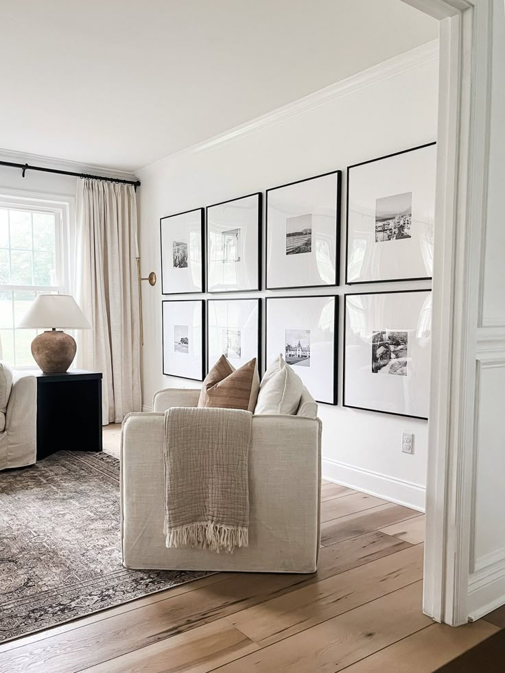 a living room filled with white furniture and pictures on the wall above it's windows