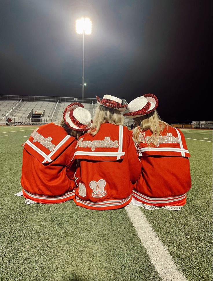 three cheerleaders sitting on the sidelines at night