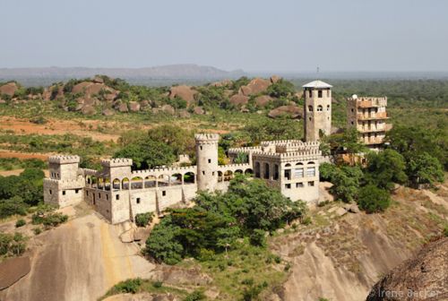 an old castle sits on top of a cliff in the middle of trees and rocks