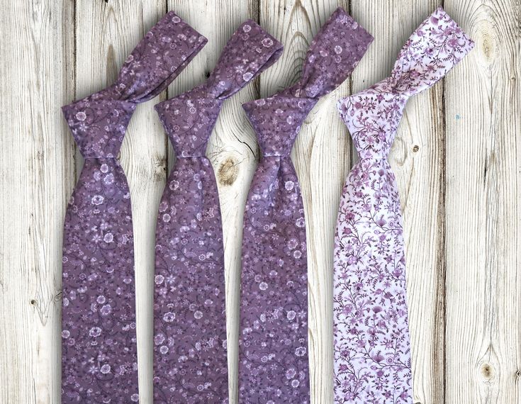 three ties are laid out on a wooden surface, one is purple and the other is white