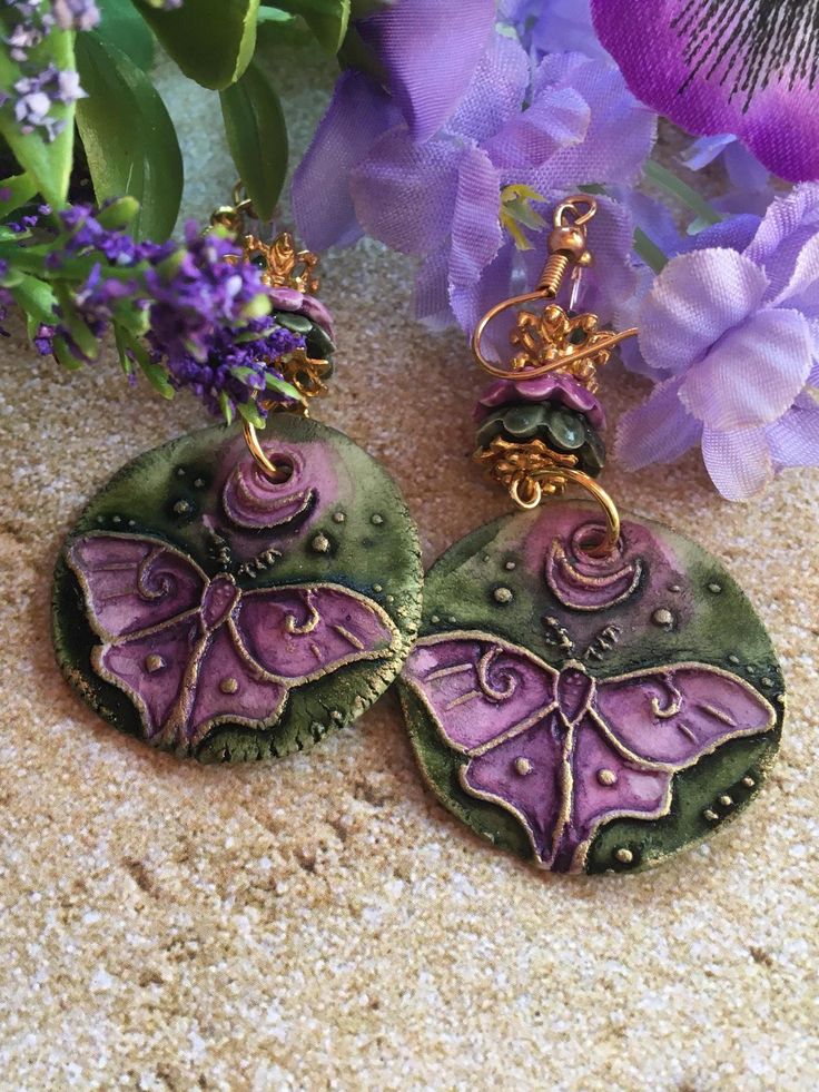 These Ceramic Earrings are made with charms made by an artisan.  Each earring has a different design and the earrings are accented with ceramic and metal flower bead caps and Swarovski crystals Handmade Bohemian Dangle Clip-on Earrings, Handmade Bohemian Drop Clip-on Earrings, Bohemian Handmade Drop Clip-on Earrings, Handmade Green Bohemian Plug Earrings, Bohemian Clip-on Earrings As Gift, Handmade Artisan Purple Earrings, Handmade Green Pendant Earrings, Artistic Polymer Clay Earrings For Pierced Ears, Bohemian Dangle Clip-on Earrings As Gift