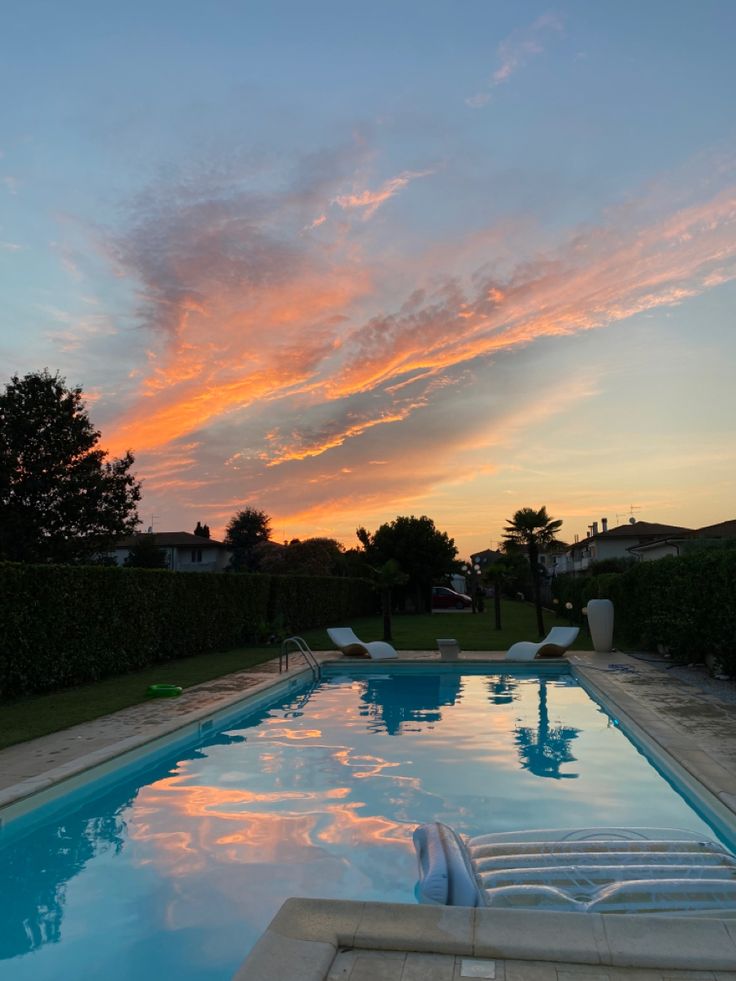 an empty swimming pool with lounge chairs in the foreground and a sunset behind it