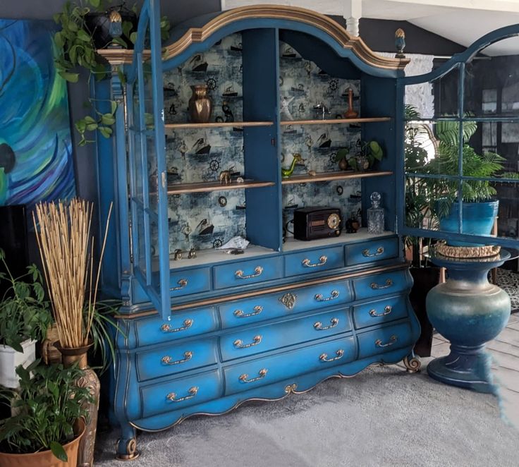 a blue china cabinet sitting in the middle of a room next to potted plants