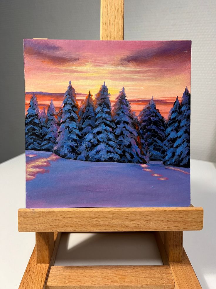 an easel with a painting on it that has snow covered trees in the background