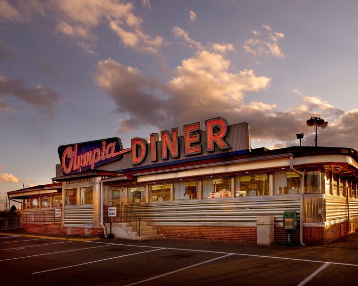 an empty parking lot in front of a diner with the sun setting on it's roof