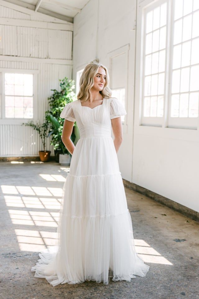 a woman wearing a white dress standing in an empty room with sunlight streaming through the windows