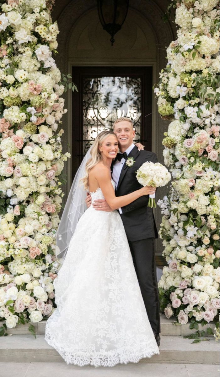 a bride and groom posing for a photo in front of a floral arch with flowers