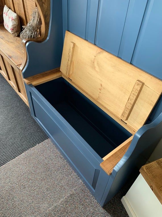 a wooden bench with an open storage compartment on the top and bottom, in front of a blue painted wall