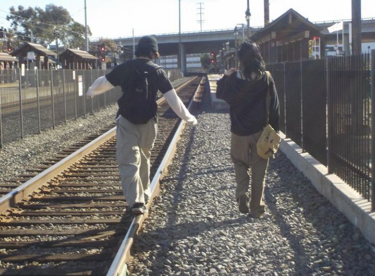 two people are walking down the railroad tracks