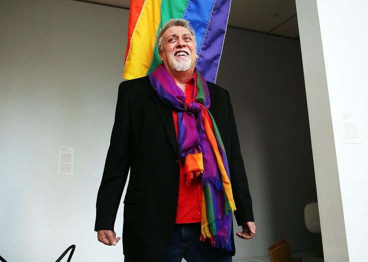 an older man standing in front of a rainbow flag