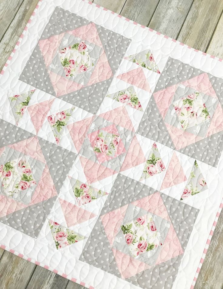 a pink and gray quilted table topper with flowers on it, sitting on a wooden surface