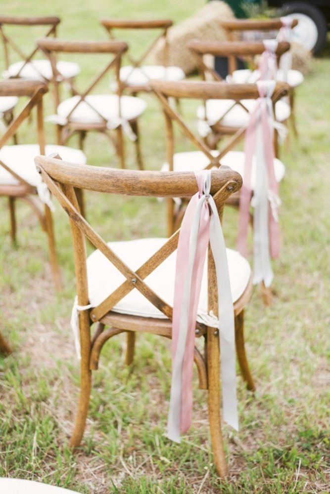 rows of wooden chairs with pink ribbons tied to them in the grass at an outdoor ceremony