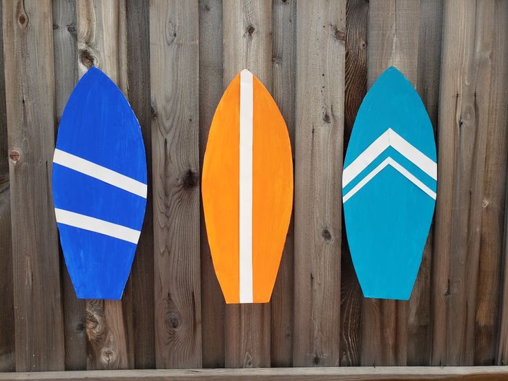 three surfboards are lined up against a wooden fence, one is blue and the other is orange