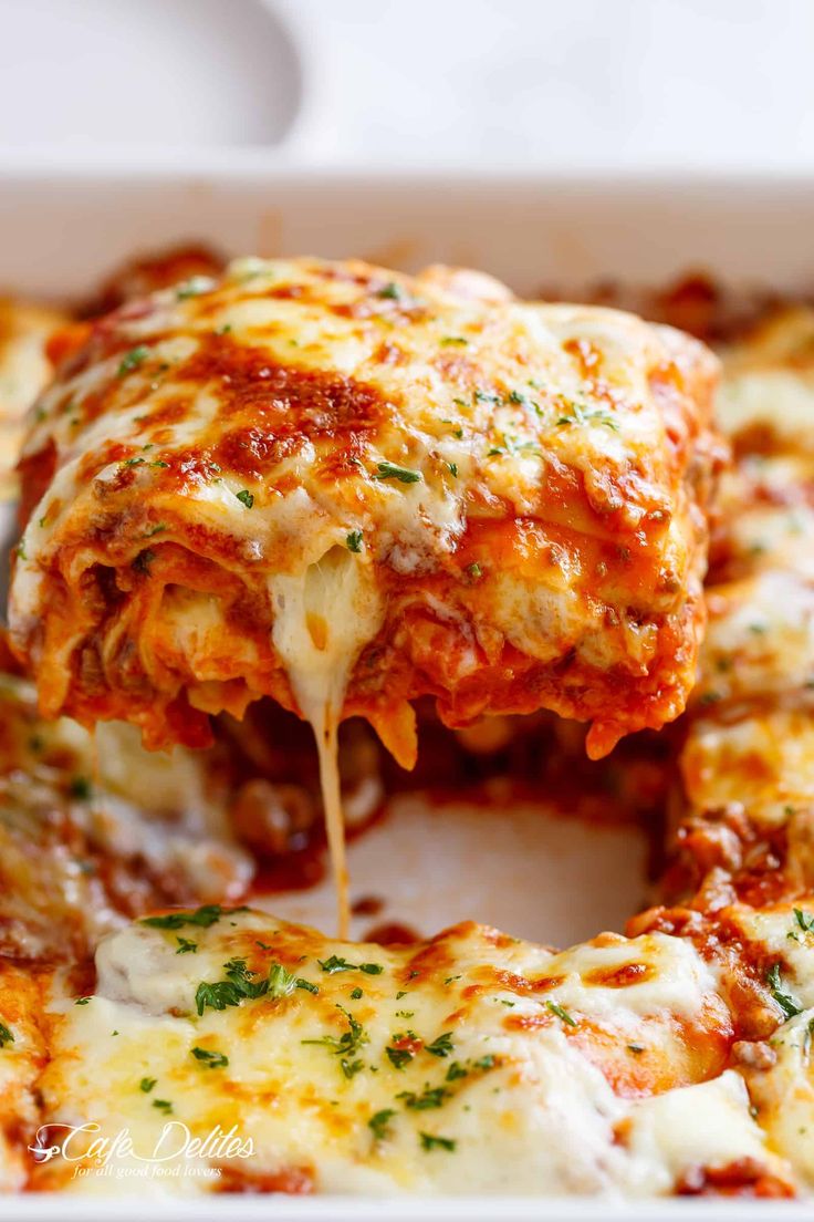 a piece of lasagna being lifted from a casserole dish with cheese and sauce