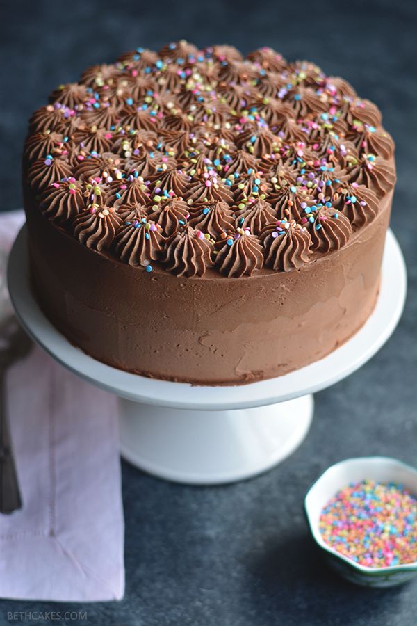 a chocolate cake with sprinkles on top sitting on a plate next to a spoon