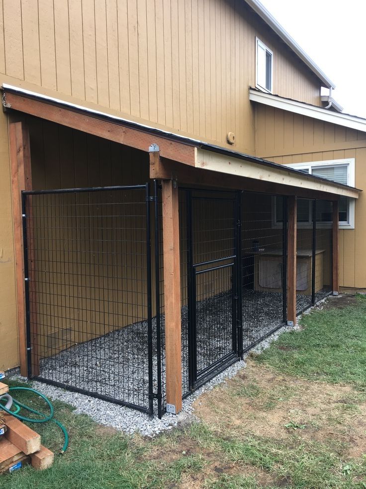 a dog kennel in front of a house with a fence around it and grass on the ground