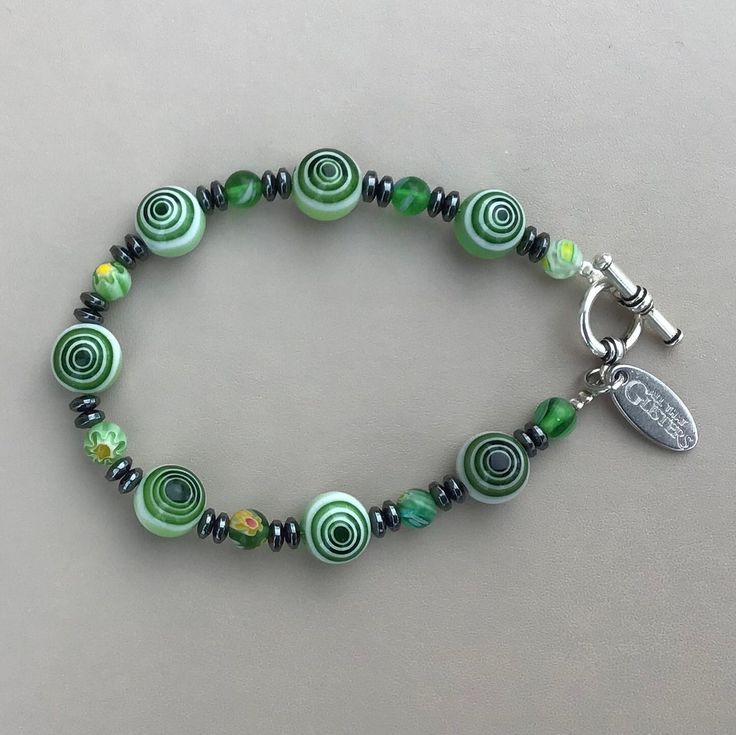 "This beautiful green Millefiori Glass and Hematite Bracelet is designed and made in Ireland. The toggle clasp is pewter. The bracelet is 8\" in length, is made on wire and has a toggle clasp. The bracelet can be made longer or shorter. There are also matching necklace options. Millefiori Glass is a type of mosaic glassware characterised by a flowerlike pattern. The term millefiori is a combination of the Italian words Mille meaning thousand and fiord meaning flowers." Green Czech Glass Spiritual Bracelets, Artisan Green Bracelets For Jewelry Making, Nickel-free Green Beaded Bracelets, Nickel-free Green Spiritual Beaded Bracelets, Green Nickel Free Bracelets With Round Beads, Marble Bracelet, Celtic Bracelet, Obsidian Bracelet, Hematite Bracelet