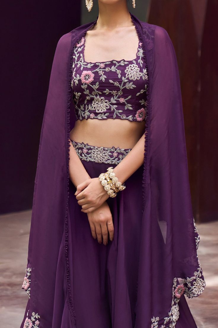 Purple skirt style lehenga with embroidered waistband. Paired with floral hand embroidered blouse and cape with scalloped floral jaal border.
Component: 3
Pattern: Embroidered
Type Of Work: Floral Motifs
Neckline: Square
Sleeve Type: Blouse: Sleeveless
Fabric: Blouse: Tussar; Skirt and Cape: Organza
Color: Purple
Other Details: 
Scalloped hem cape
Asymmetric cape
Occasion: Destination Wedding - Aza Fashions Cape Organza, Asymmetric Cape, Hand Embroidered Blouse, Cape Set, Embroidered Lehenga, Purple Skirt, Blouse Sleeveless, Purple Blouse, Skirt Style