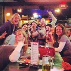 a group of women sitting at a table with beers in front of them and smiling