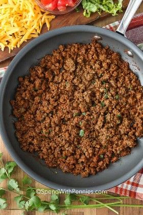 ground beef in a skillet with cheese, tomatoes and lettuce on the side