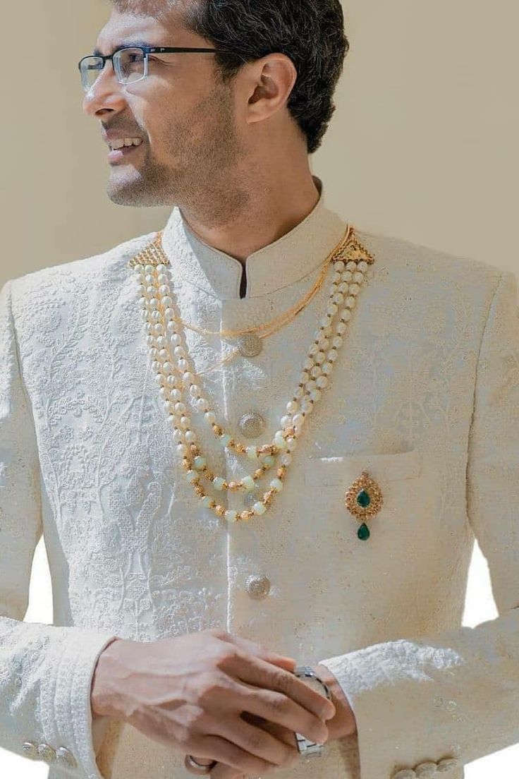 a man in a white suit and pearls necklace