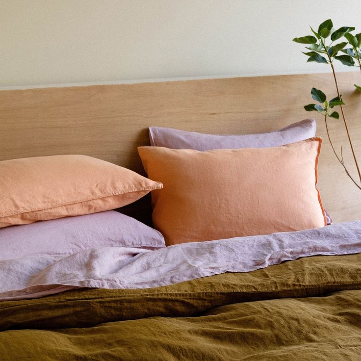 a bed topped with pillows and blankets next to a plant on top of a wooden headboard