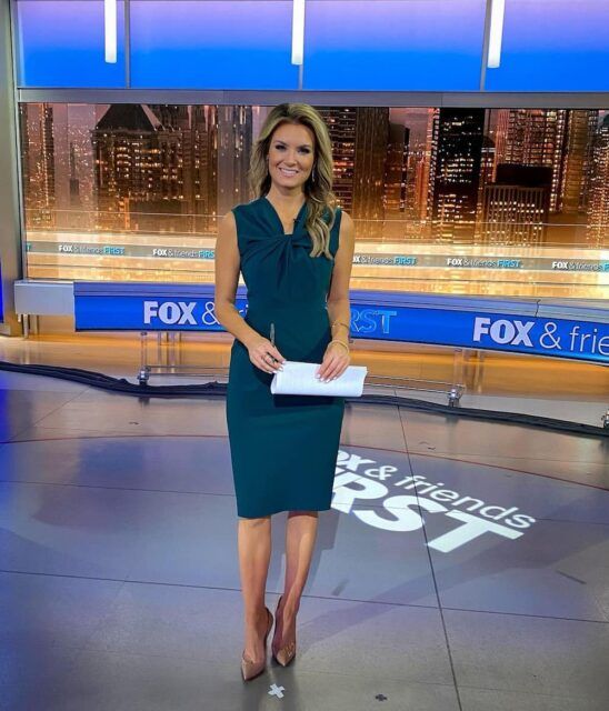 a woman in a green dress is standing on the news set with her handbag