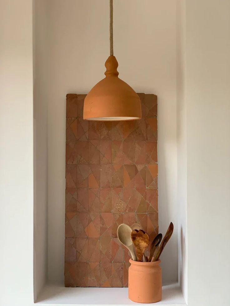 an orange pot with utensils in it on a shelf next to a light fixture