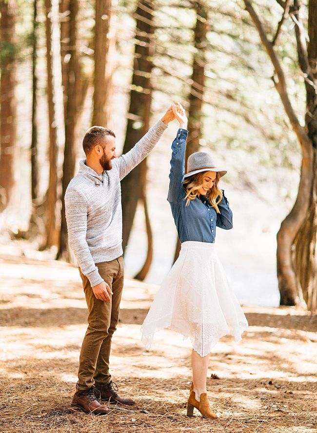 a man and woman standing in the woods with their arms raised up to each other