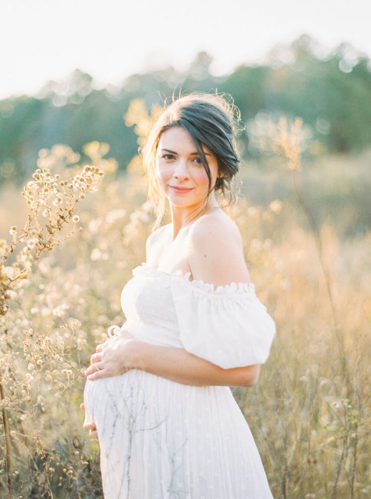 a pregnant woman in a white dress standing in tall grass