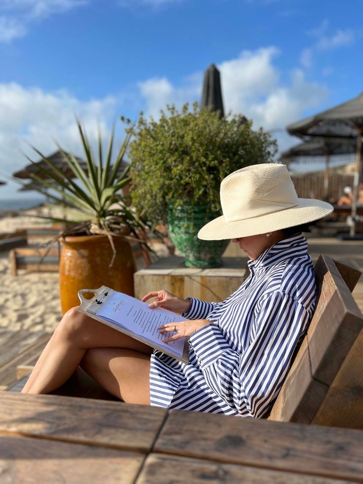 a woman in a hat sitting on a bench with a book and pen next to her