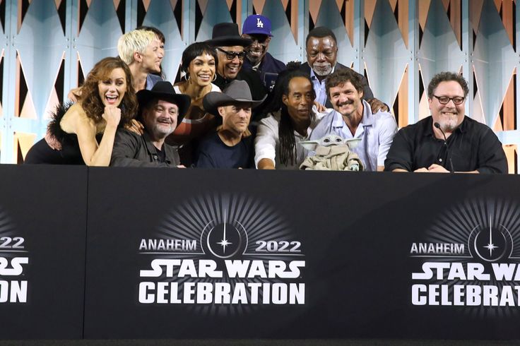 a group of people standing next to each other at a star wars celebration in front of a wall