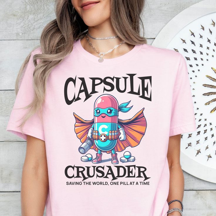 Order by 12/12/24 to ensure Christmas delivery. Orders will be accepted after this date and will be processed as soon as possible, but may not arrive before Christmas Day. Please plan accordingly as refunds will not be provided for orders that are delivered within their estimated window. Unleash your inner hero with our "Capsule Crusader: Saving the World One Pill at a Time" shirt! Perfect for pharmacists and pharmacy techs, this funny and spooky Halloween costume tee adds a superhero twist to y Themed Pink Tops With Letter Print, Superhero Cartoon Print Crew Neck Top, Pink Themed Crew Neck Tops, Pink Crew Neck Themed Tops, Superhero Crew Neck Top With Front Print, Superhero Crew Neck Top With Letter Print, Superhero Fan Merchandise Tops With Letter Print, Superhero Letter Print Tops For Fan Merchandise, Superhero Letter Print Tops As Fan Merchandise