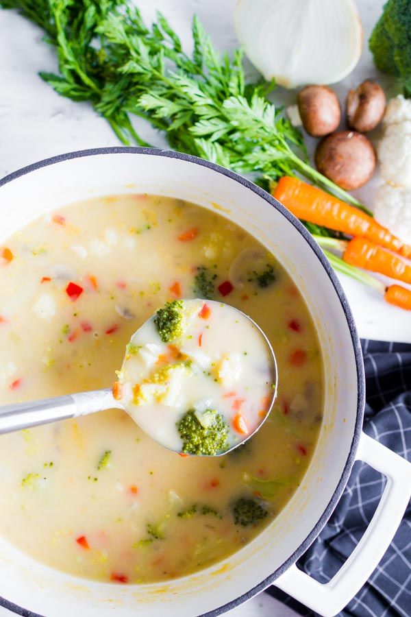 a bowl of soup with broccoli, carrots and cauliflower on the side