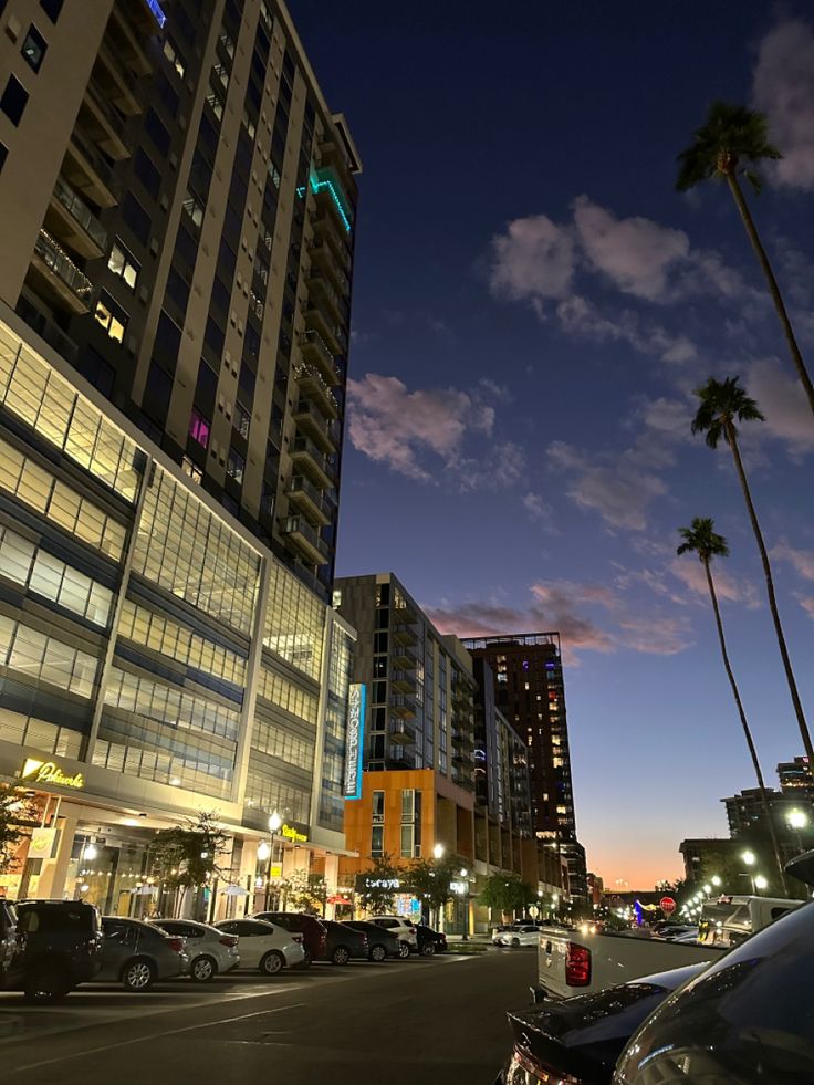 cars are parked on the street in front of tall buildings and palm trees at night