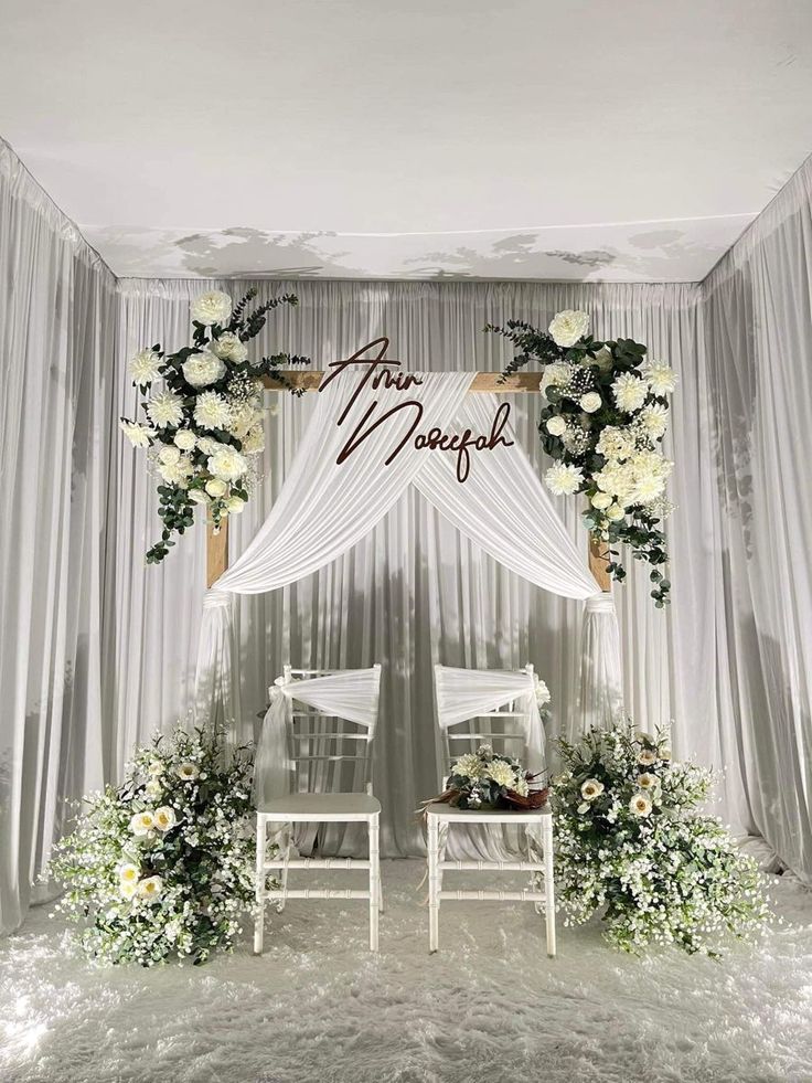 two white chairs sitting under a wedding arch