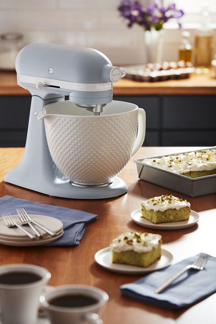 a kitchen table with plates and cups on it, including a cake stand mixer in the middle