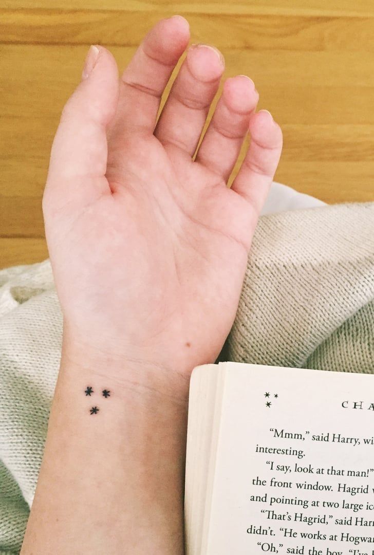 a woman's hand with a tiny star tattoo on her left wrist next to an open book