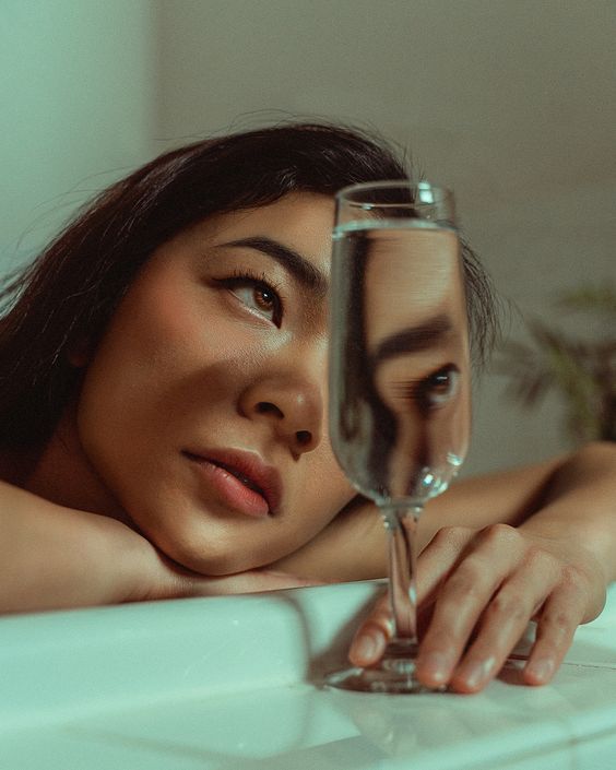 a woman leaning on a bath tub with a glass of wine in front of her