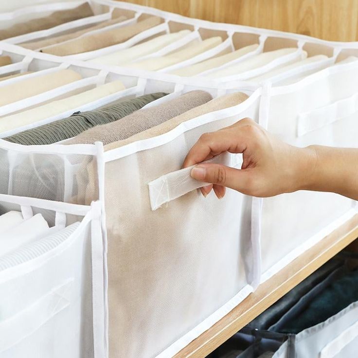 a person is picking up some clothes from a drawer with their hand on the bottom shelf