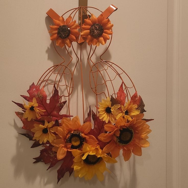 a metal wreath with sunflowers and leaves hanging on a white wall next to a door