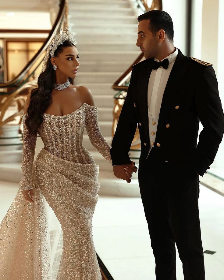 a man in a tuxedo and a woman in a gown hold hands as they walk down the stairs