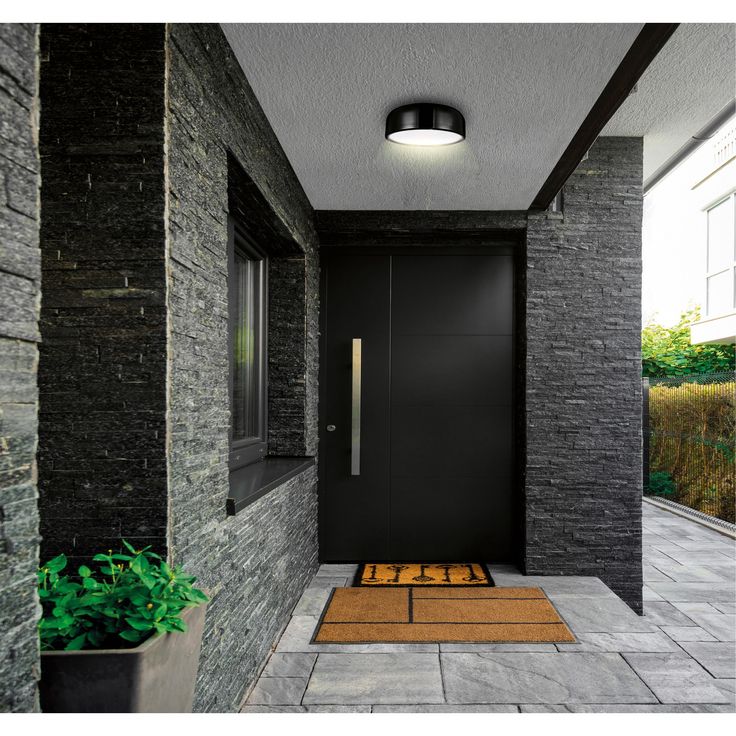 a black door with a yellow mat on the floor in front of it and a potted plant next to it