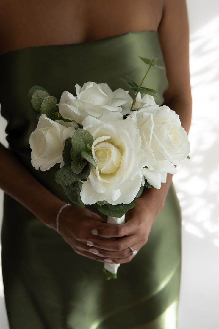 a woman in a green dress holding a bouquet of white roses