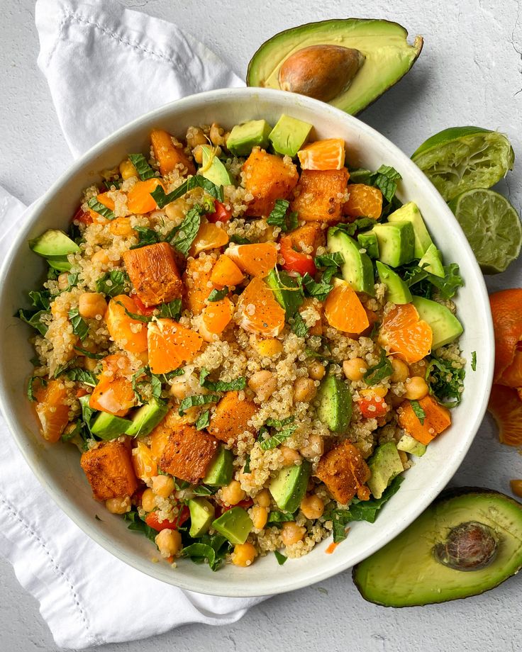 a white bowl filled with rice, carrots and avocado slices next to sliced oranges